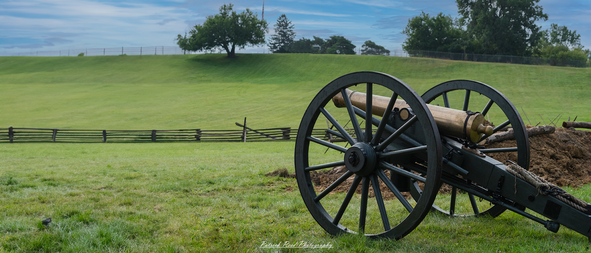 A cannon positioned on a rise, overlooking an expansive field. The scene captures the historical significance of the artillery piece, with the barrel pointed toward the horizon, symbolizing the readiness for battle and the strategic importance of the location.